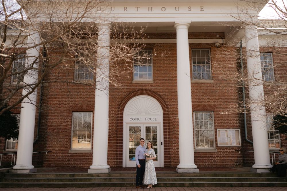 A historic red brick courthouse with white columns creates an elegant backdrop for a ceremony on the steps.