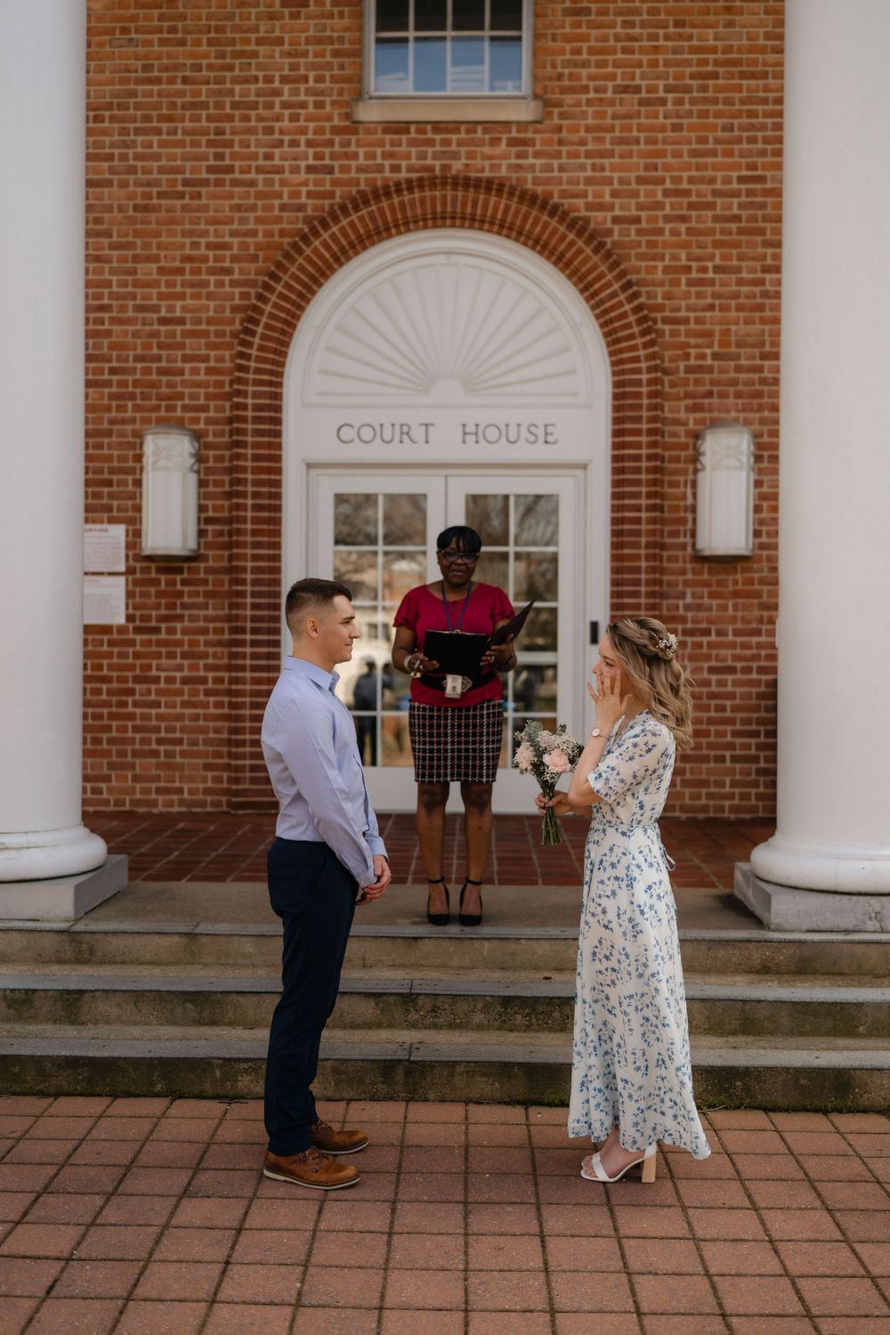 A courthouse ceremony taking place on brick steps under an arched entrance with white columns.