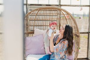 A series of three photos showing a mother and her baby sitting in a decorative wicker chair with pink cushions in a bright greenhouse.