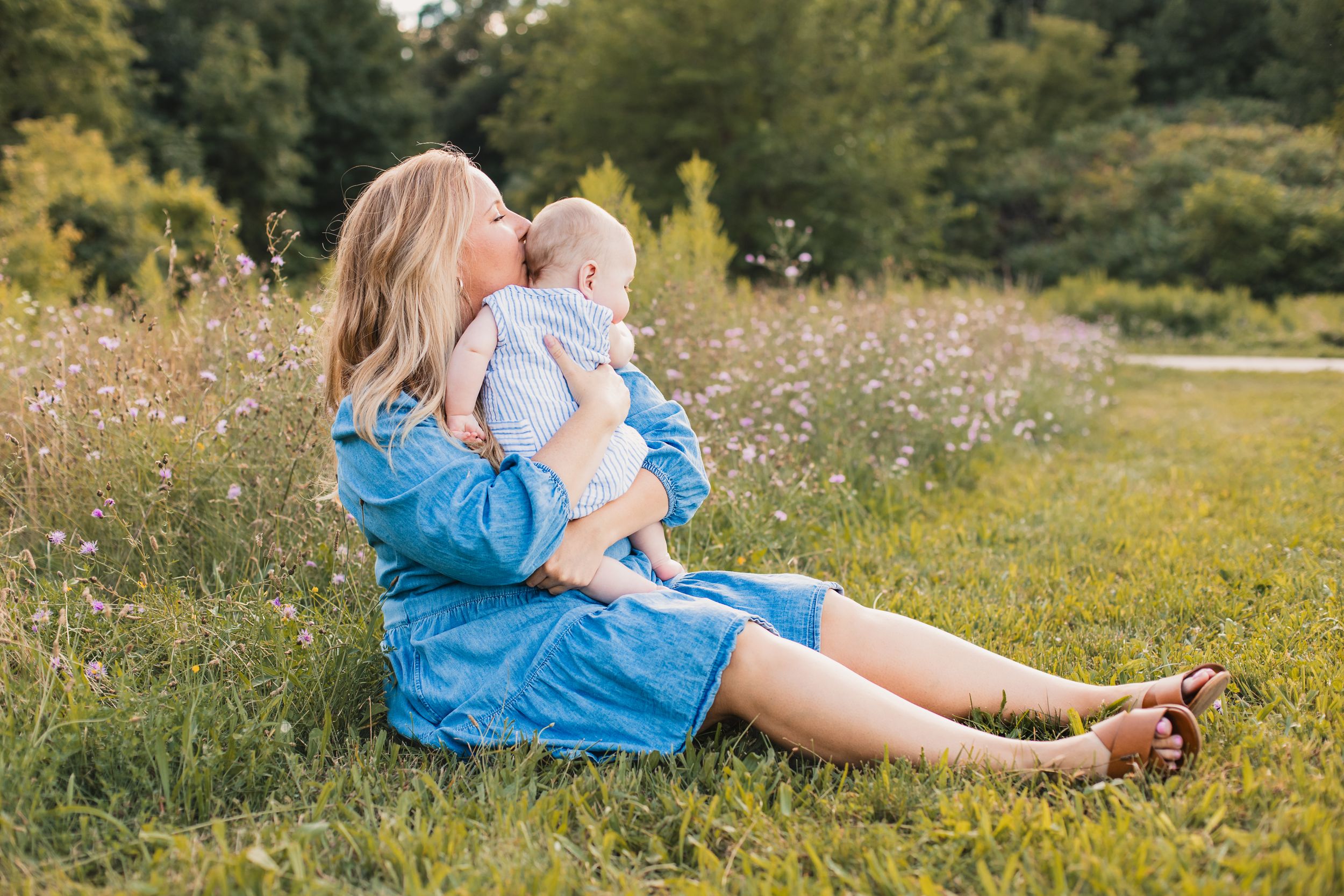 A series of photos showing someone in blue sitting in a wildflower meadow on a sunny summer day holding their baby.