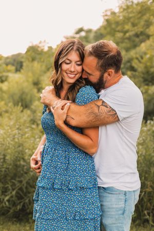 A couple shares a tender embrace outdoors, with the person wearing a blue floral dress against a natural green background.