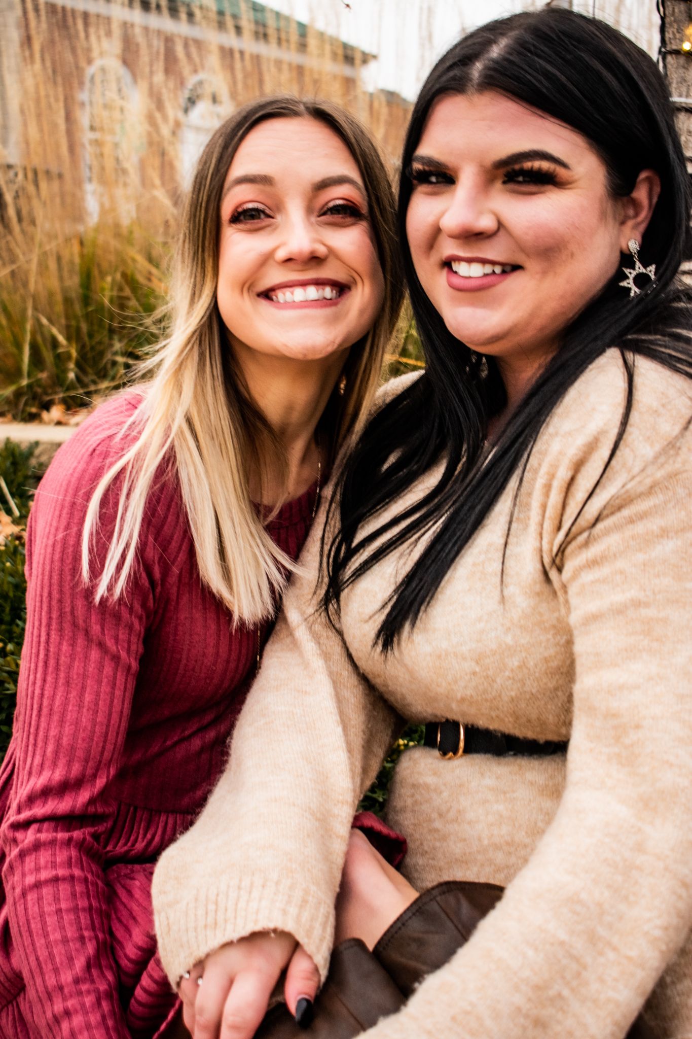 Friends in burgundy and beige sweaters share a close moment outdoors during winter.