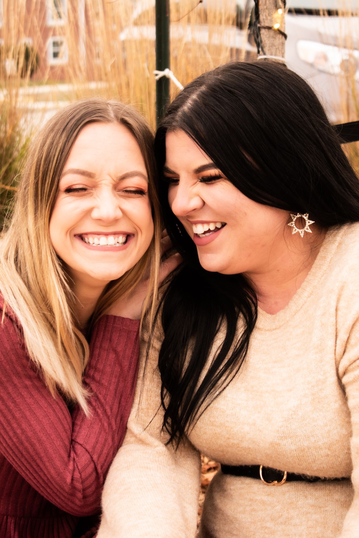 Two friends in winter sweaters share a genuine laugh during an outdoor photoshoot.