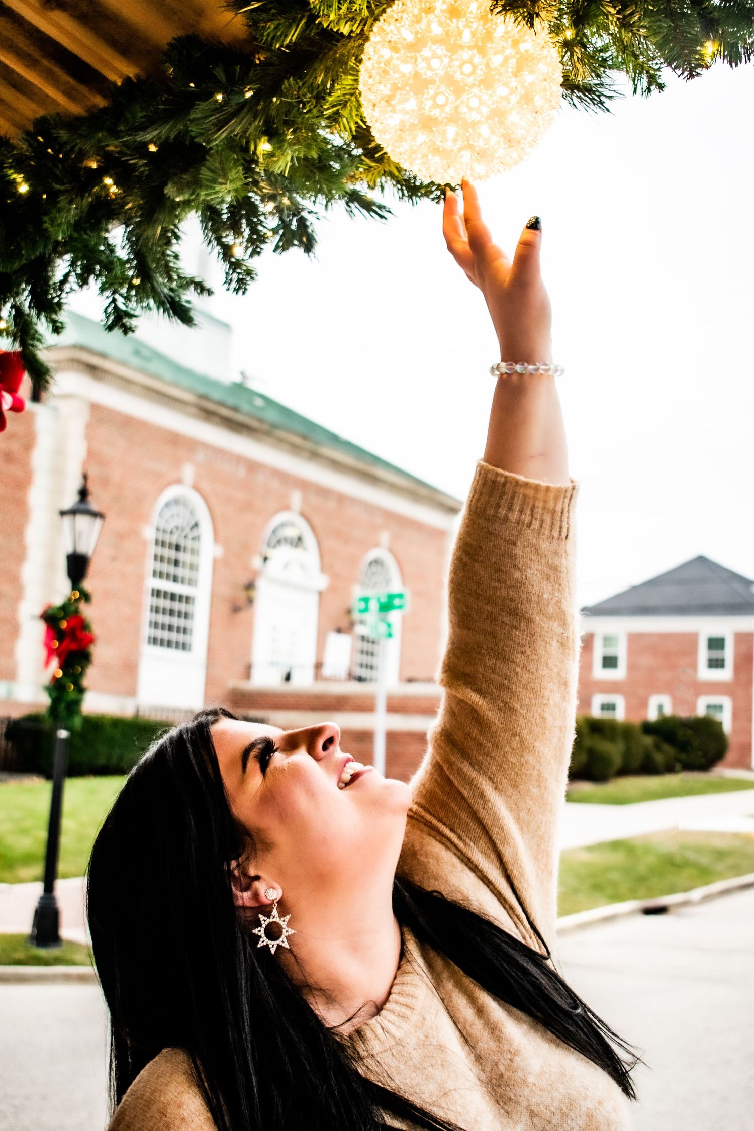 Person reaching up to touch a glowing Christmas ornament decoration outside a brick church building.