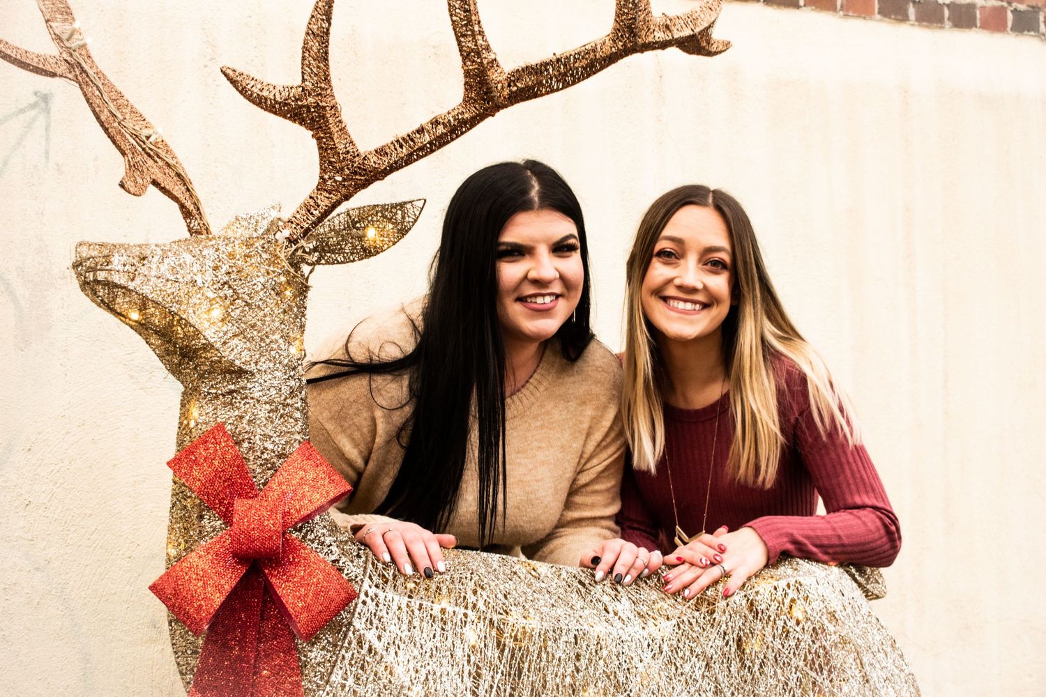 Two friends posing together with a sparkly gold reindeer holiday decoration.
