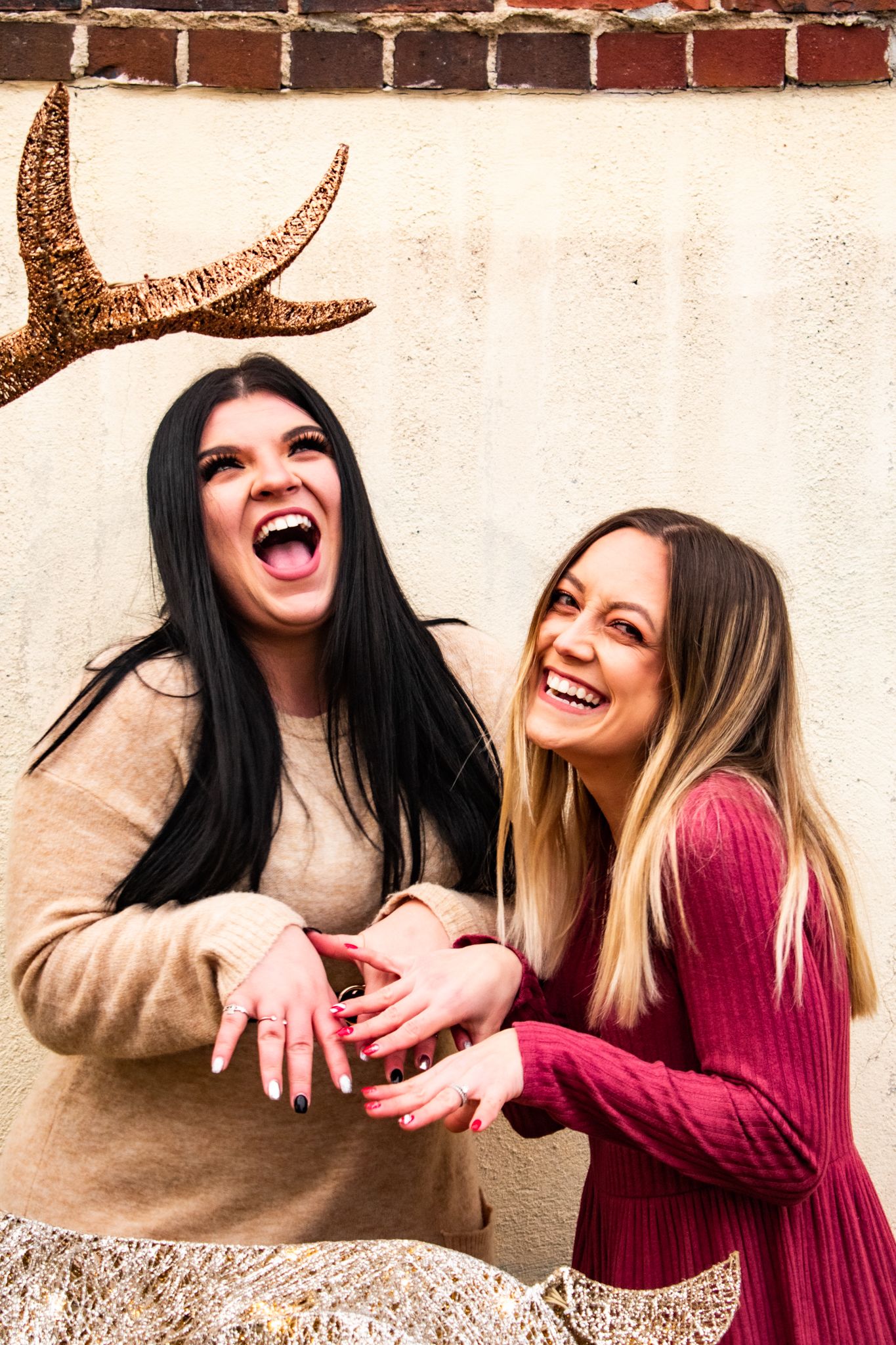 Two friends laughing together while posing with festive golden reindeer antler decorations.