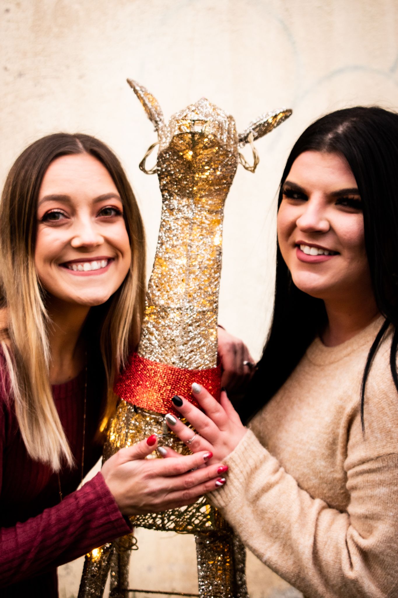 Two friends holding a glittery gold Christmas reindeer decoration together and smiling.