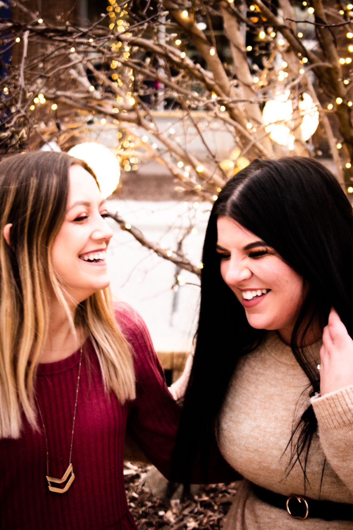 Two friends sharing genuine laughter under twinkling holiday lights outdoors.