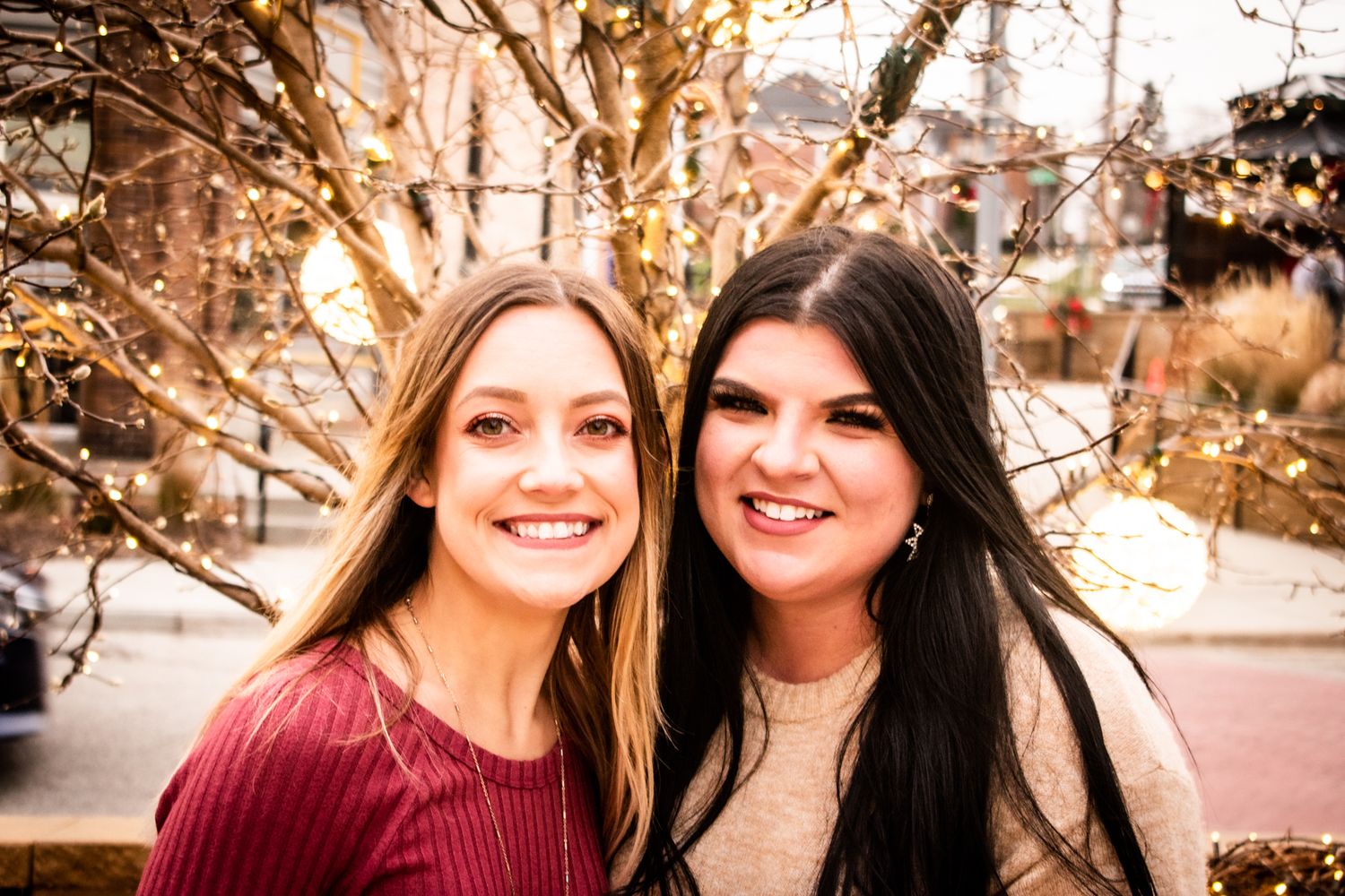 Two friends in burgundy and beige outfits smiling for a winter portrait outdoors.