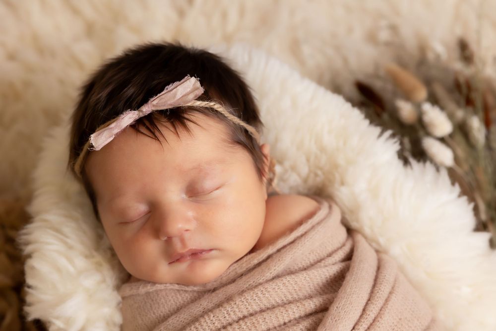 Newborn baby wrapped in beige fabric sleeping peacefully on plush white fur.
