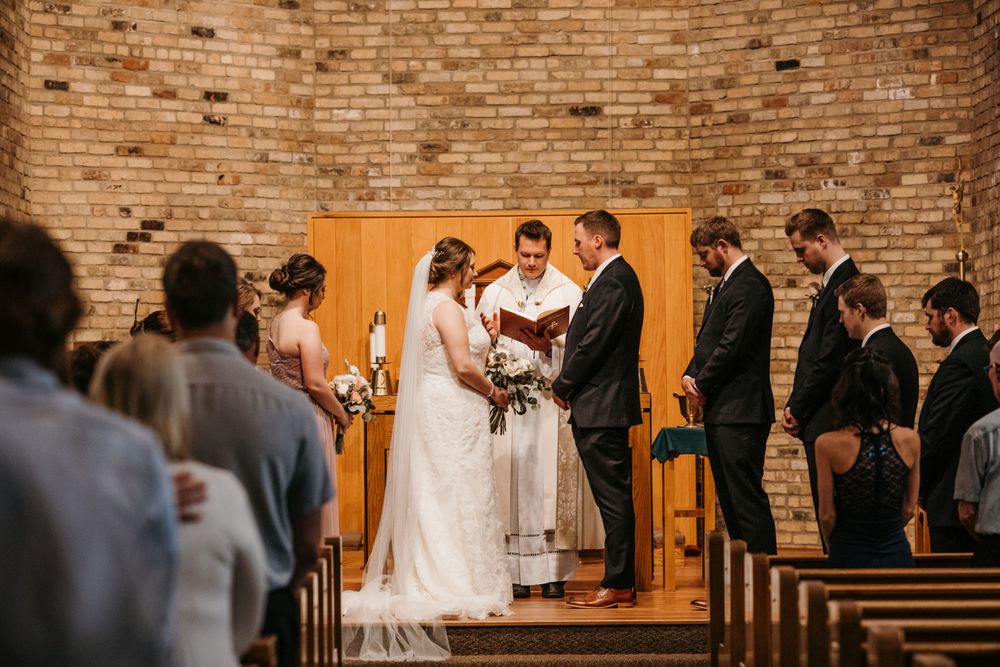 A bride and groom exchange vows at the altar with an officiant and groomsmen in a brick church.