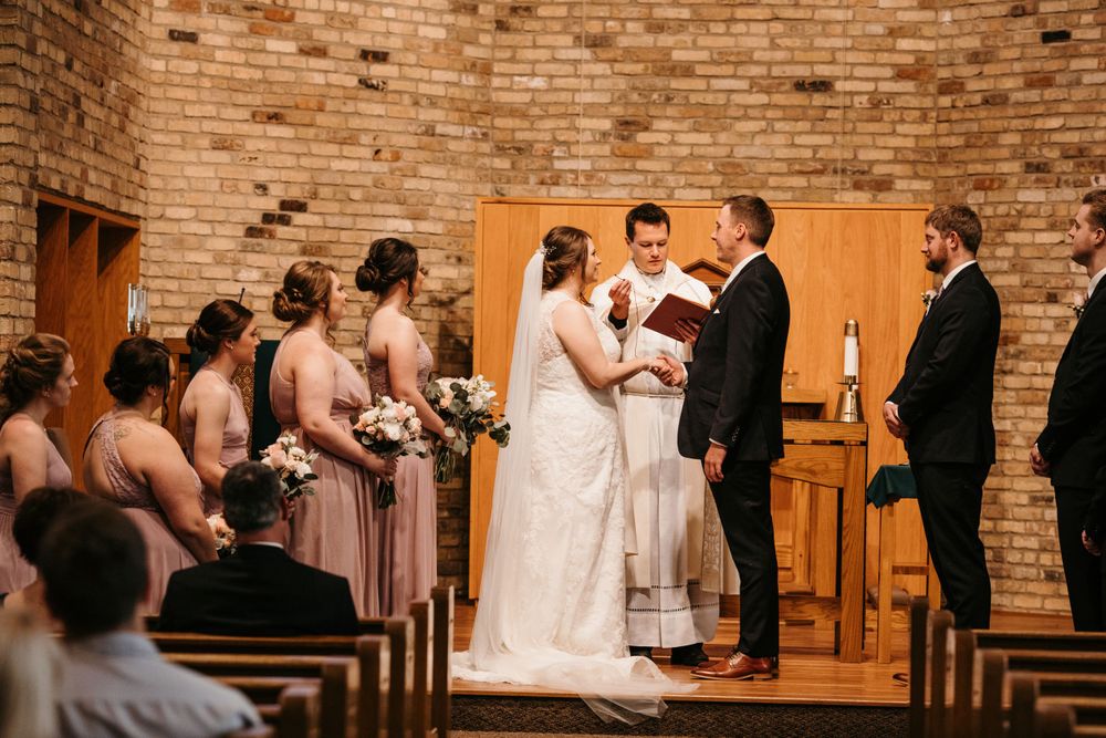 Wedding party stands at the altar as officiant reads from a red book during a church ceremony.