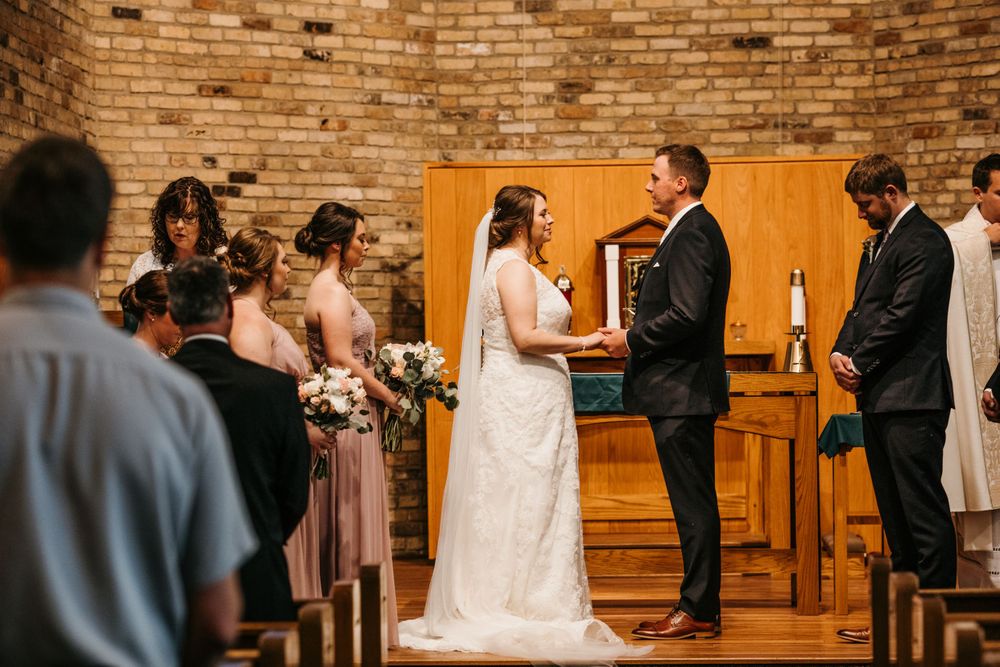 Bride and groom hold hands at the altar during their wedding ceremony in a brick church.