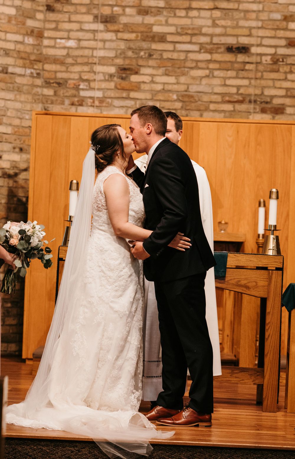 Bride and groom share their first kiss at the altar during a wedding ceremony in a brick church.