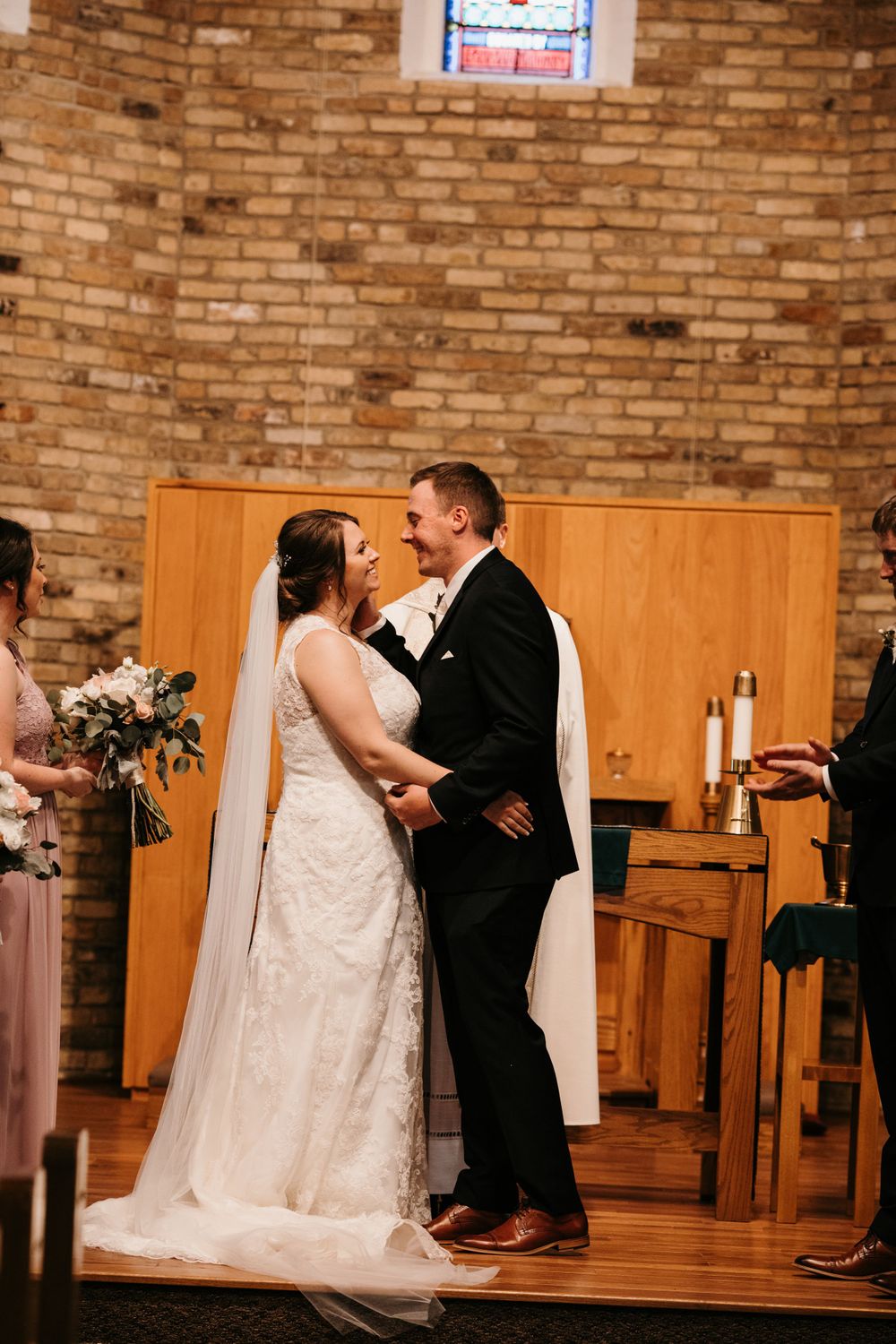 Bride and groom smile at each other after exchanging vows at the altar in a brick church.