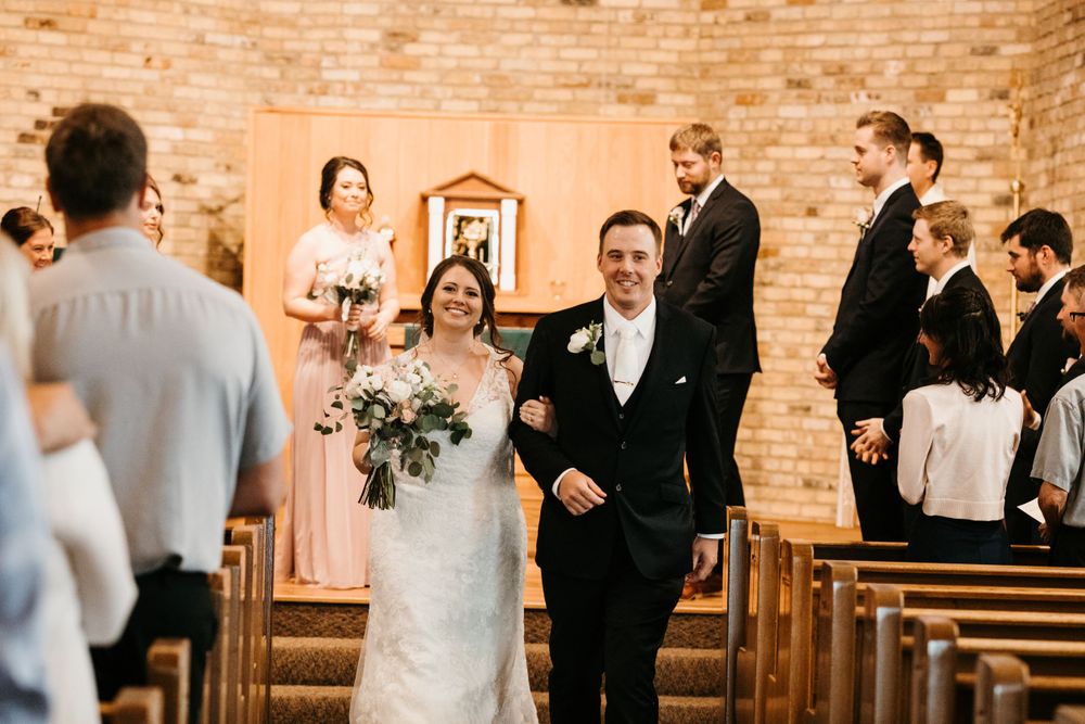 Newlyweds walk joyfully down the aisle after their wedding ceremony in a warm brick church.