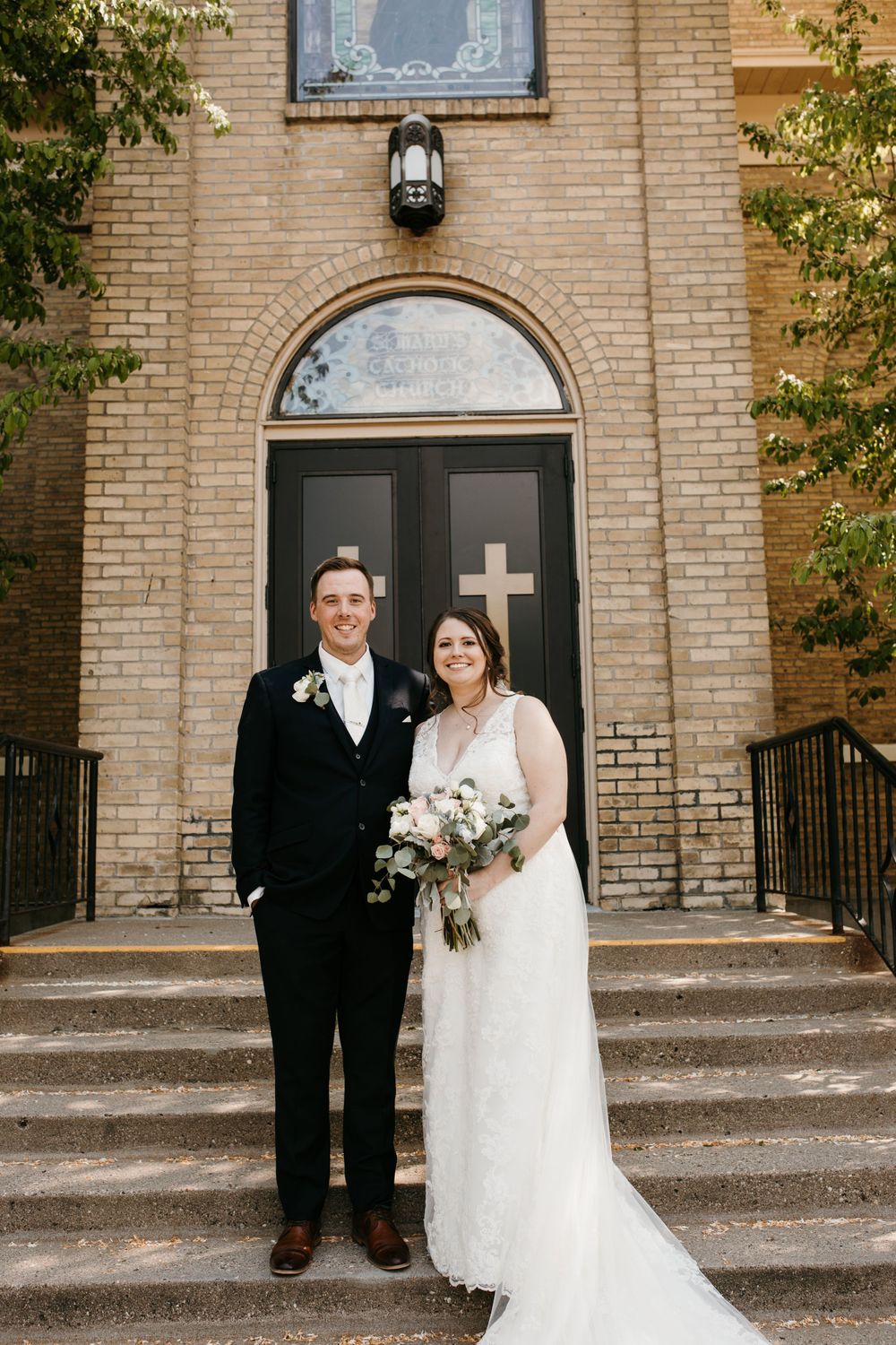 Bride and groom smiling together on church steps after wedding ceremony.