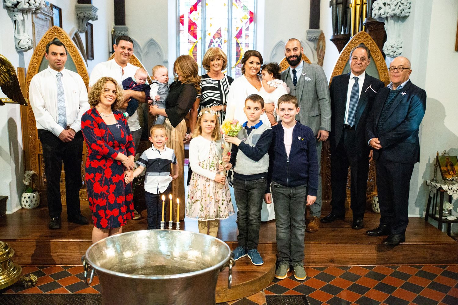 A group gathers around a baptismal font in a church interior for a christening ceremony.