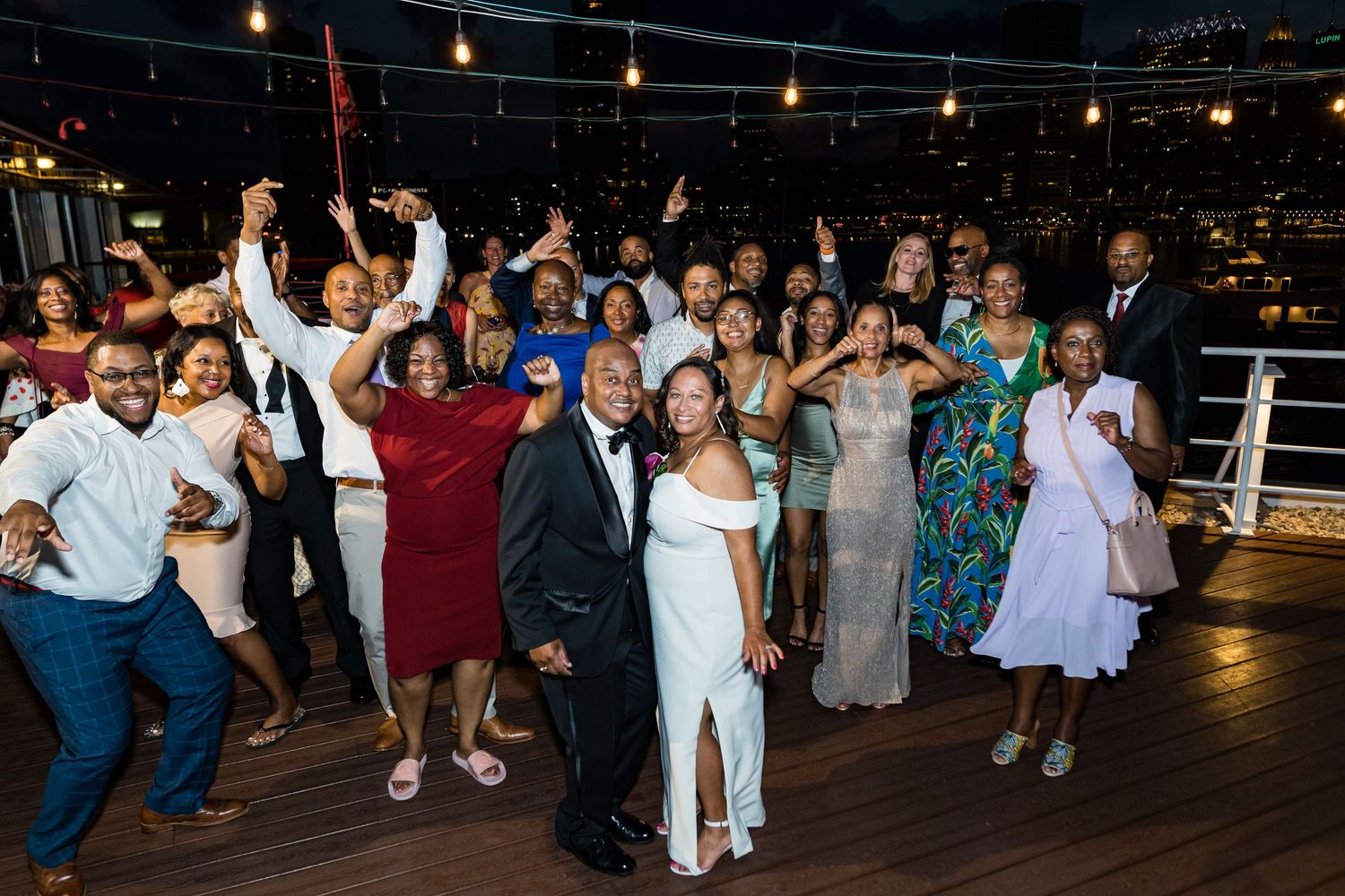 Wedding guests dancing together on a rooftop venue at night under string lights.