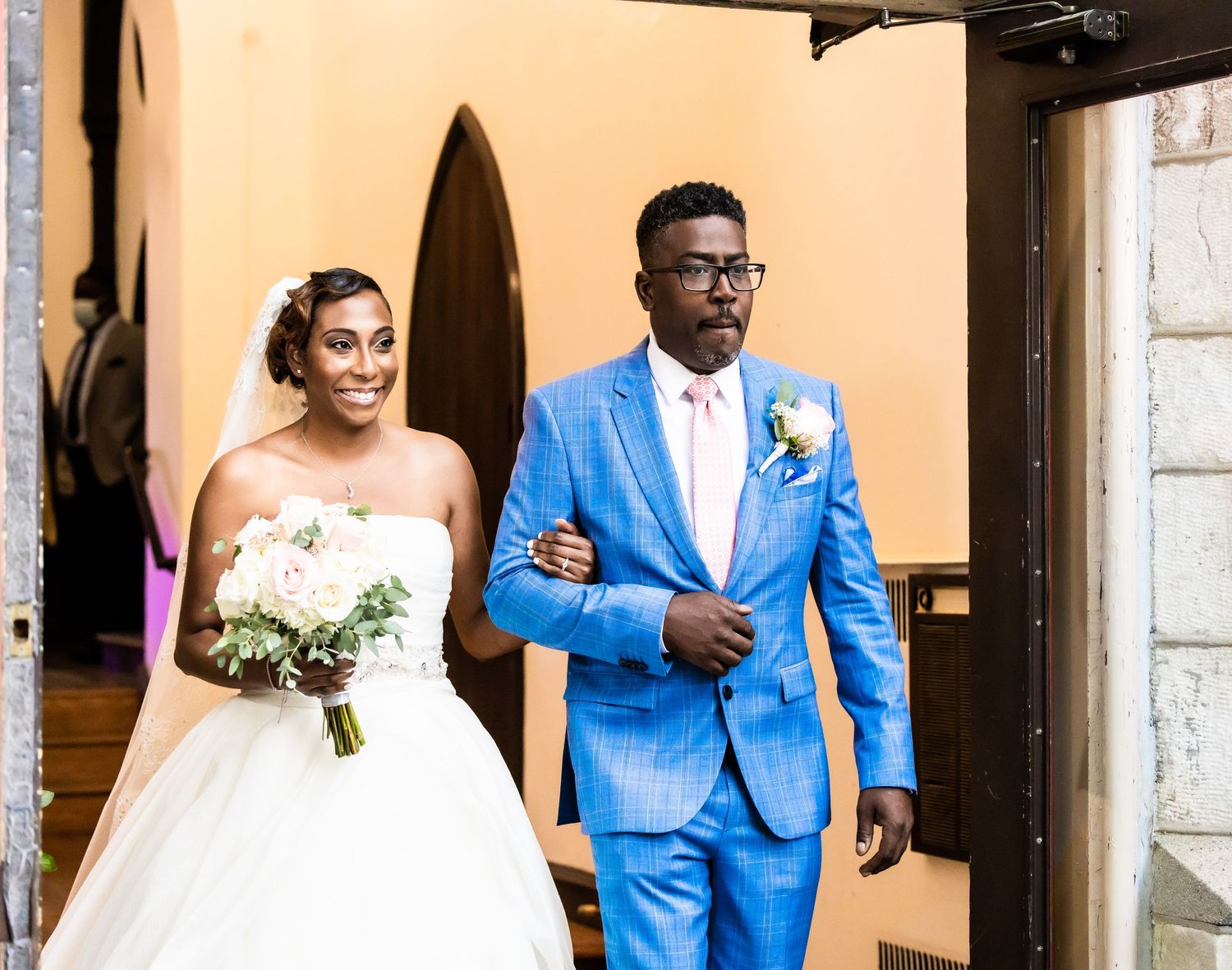 Couple exits church ceremony with bride in white gown and groom in bright blue suit.