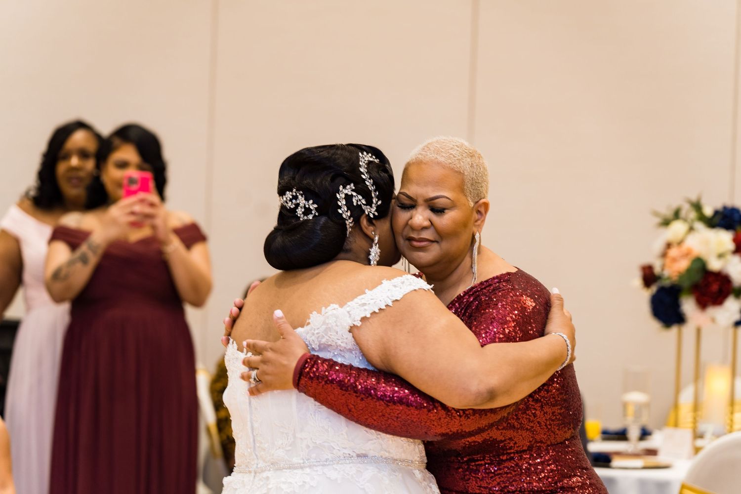 Emotional embrace during wedding reception with burgundy and white attire.