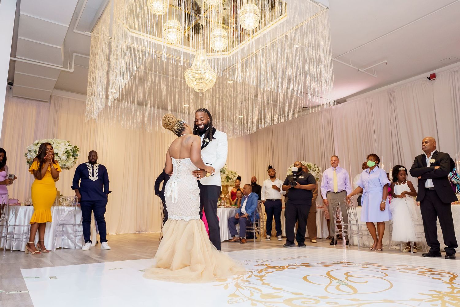Elegant wedding reception with chandelier and guests dancing on monogrammed dance floor.