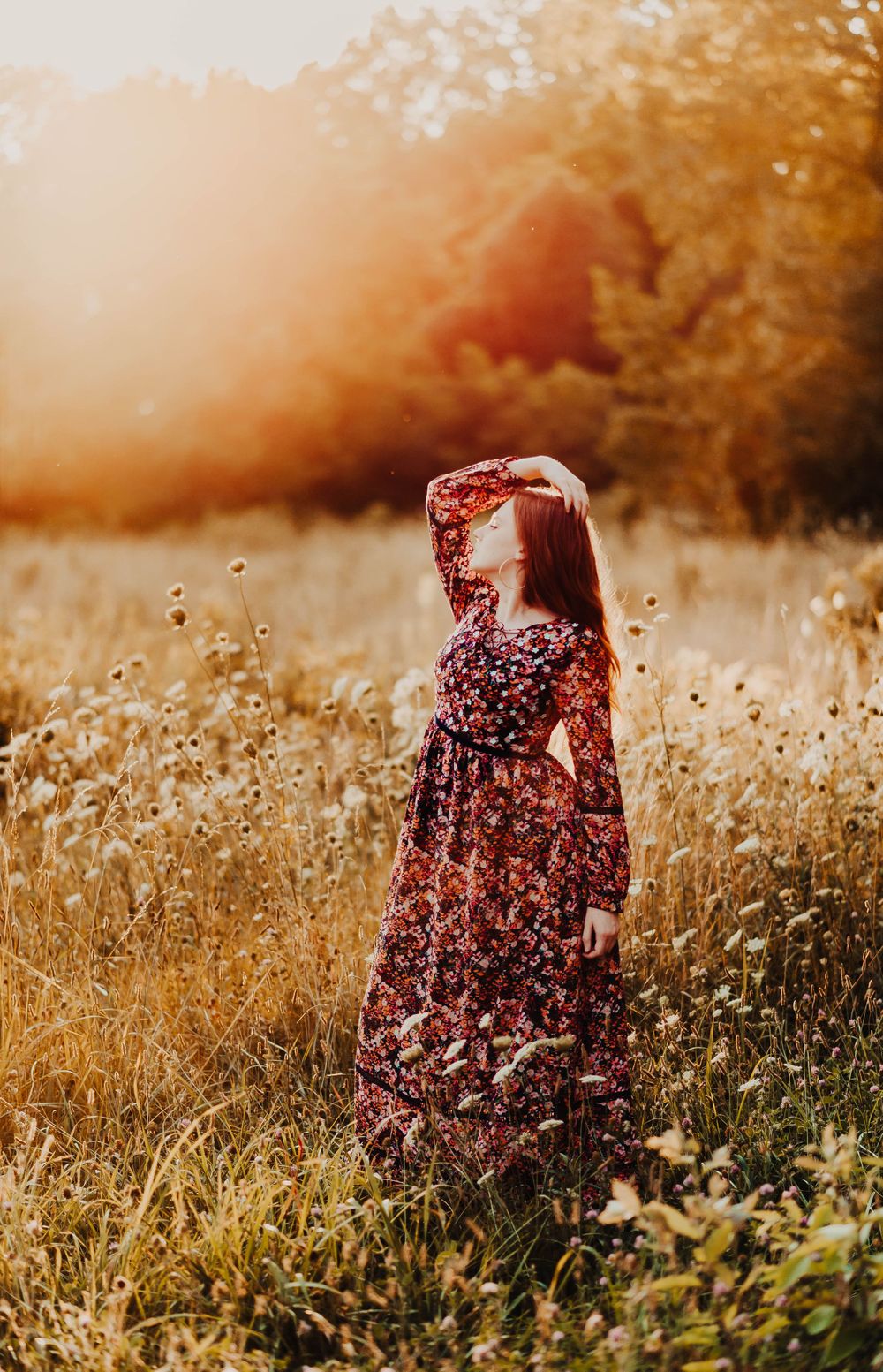 Person in floral dress walking through a sunlit meadow with wildflowers at golden hour.
