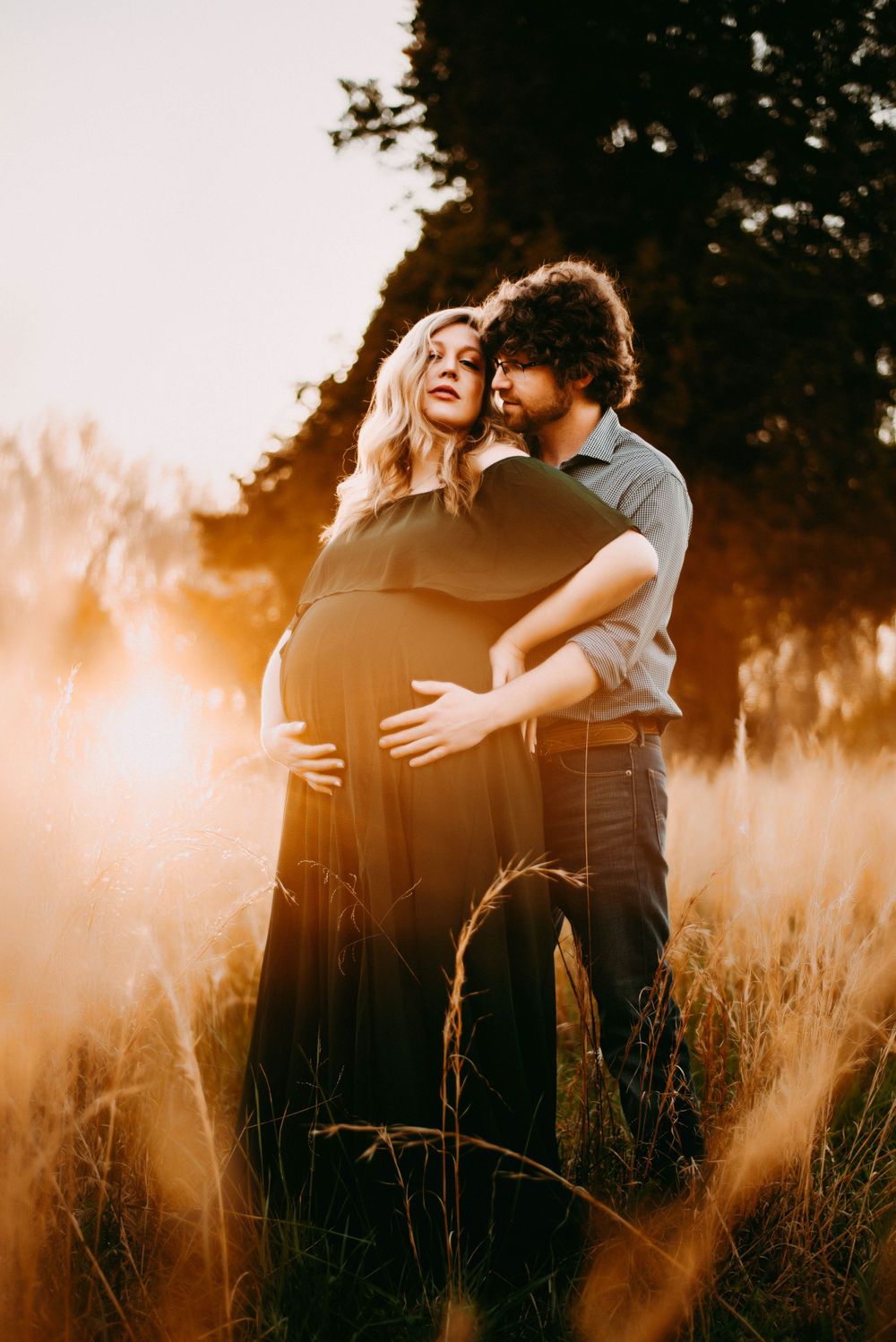 Expecting couple shares intimate moment in golden sunlit field.