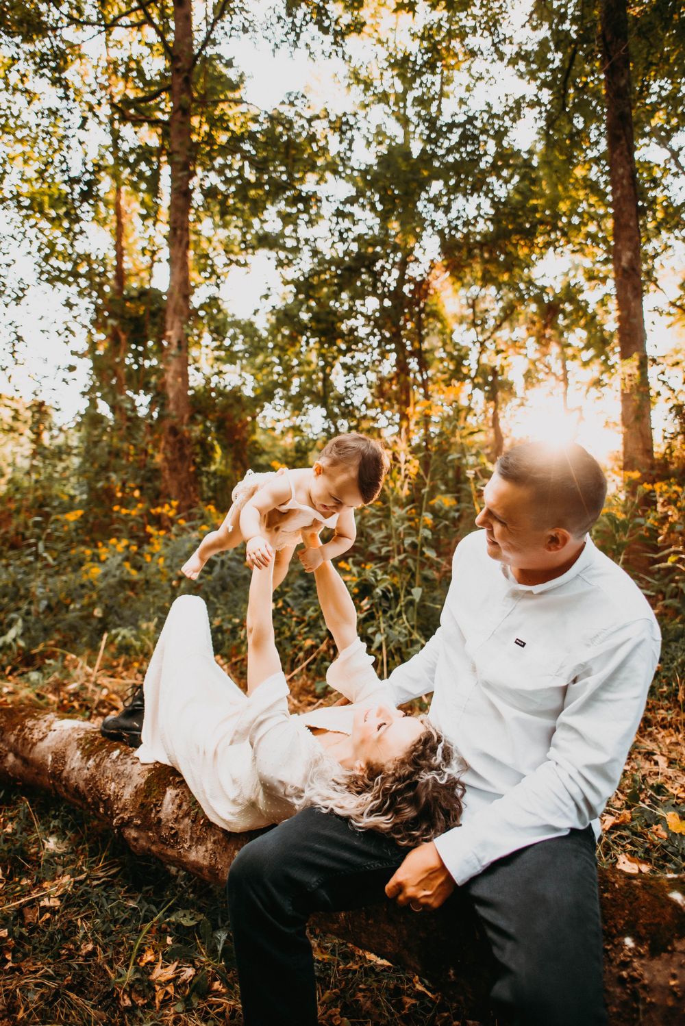 Family plays together on fallen tree trunk in sunlit forest.