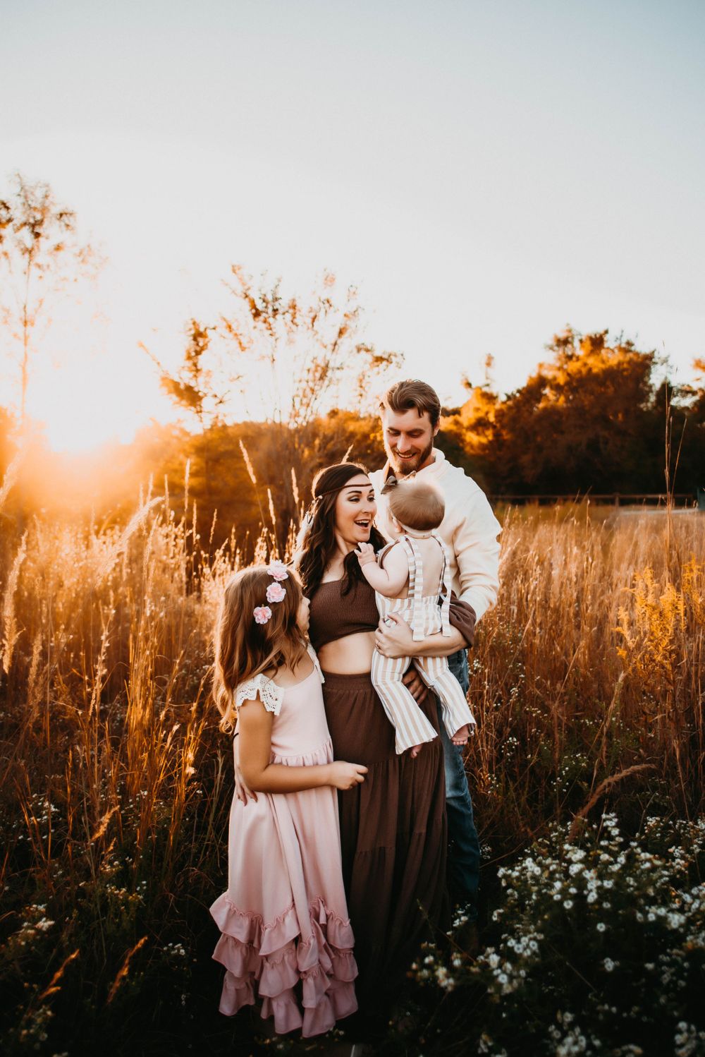 Family poses together in tall grass field during golden hour sunset.