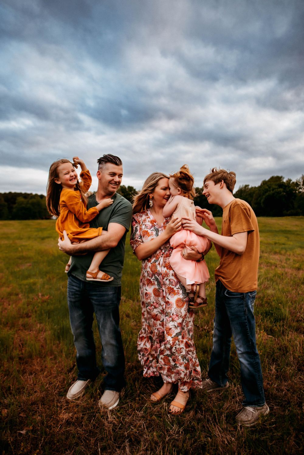 Playful family photography session in a field under dramatic cloudy skies.