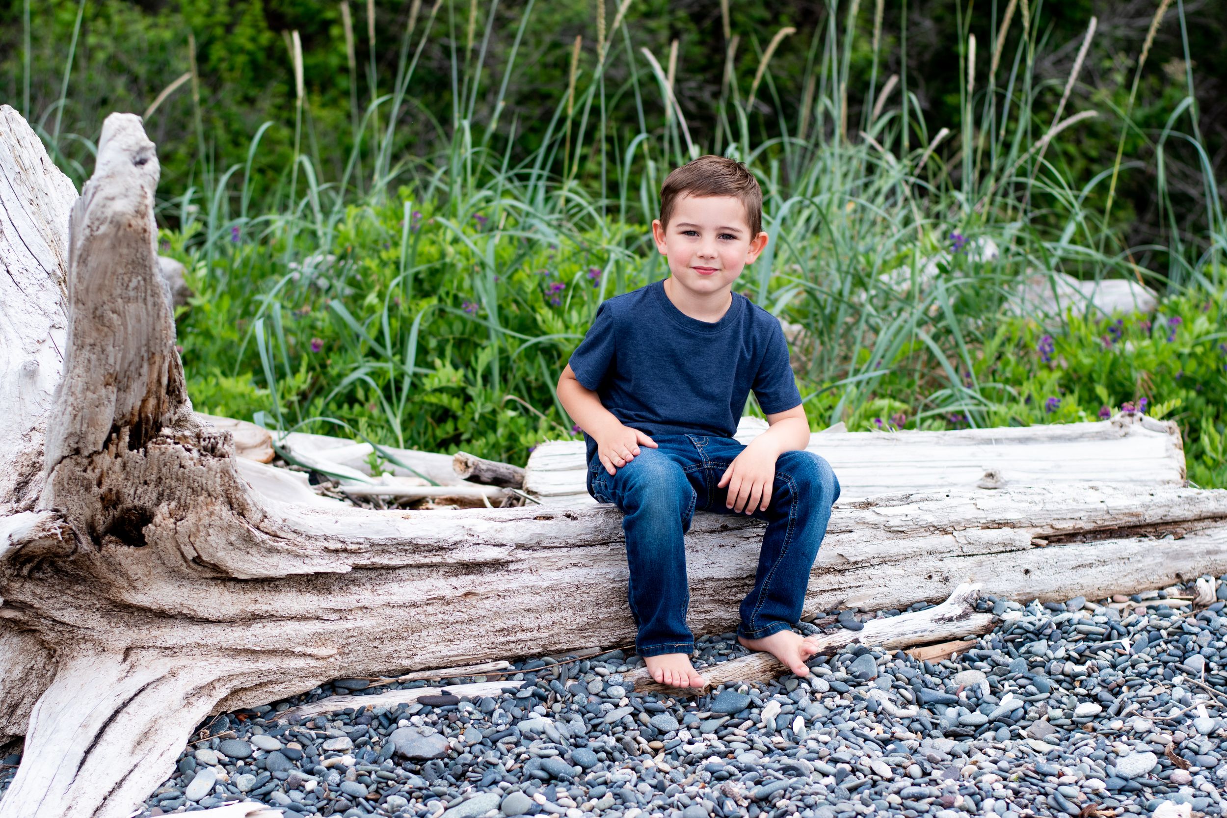 Young child sitting on a log on a rocky beach