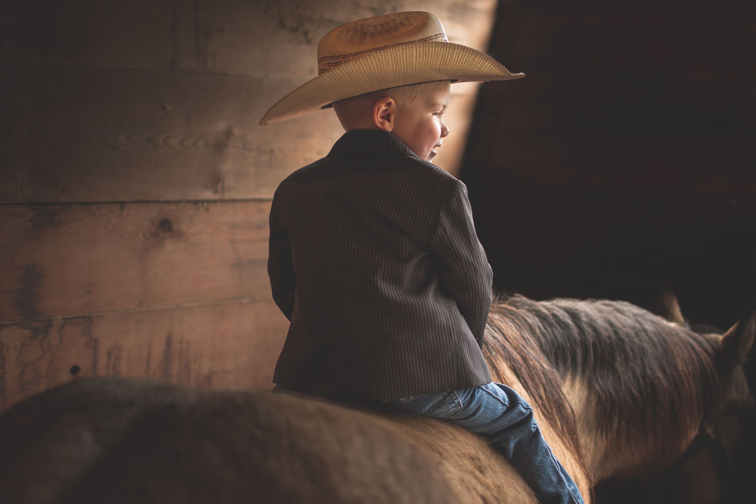 A cowboy wearing a hat and dark jacket rides horseback in dramatic moody lighting.
