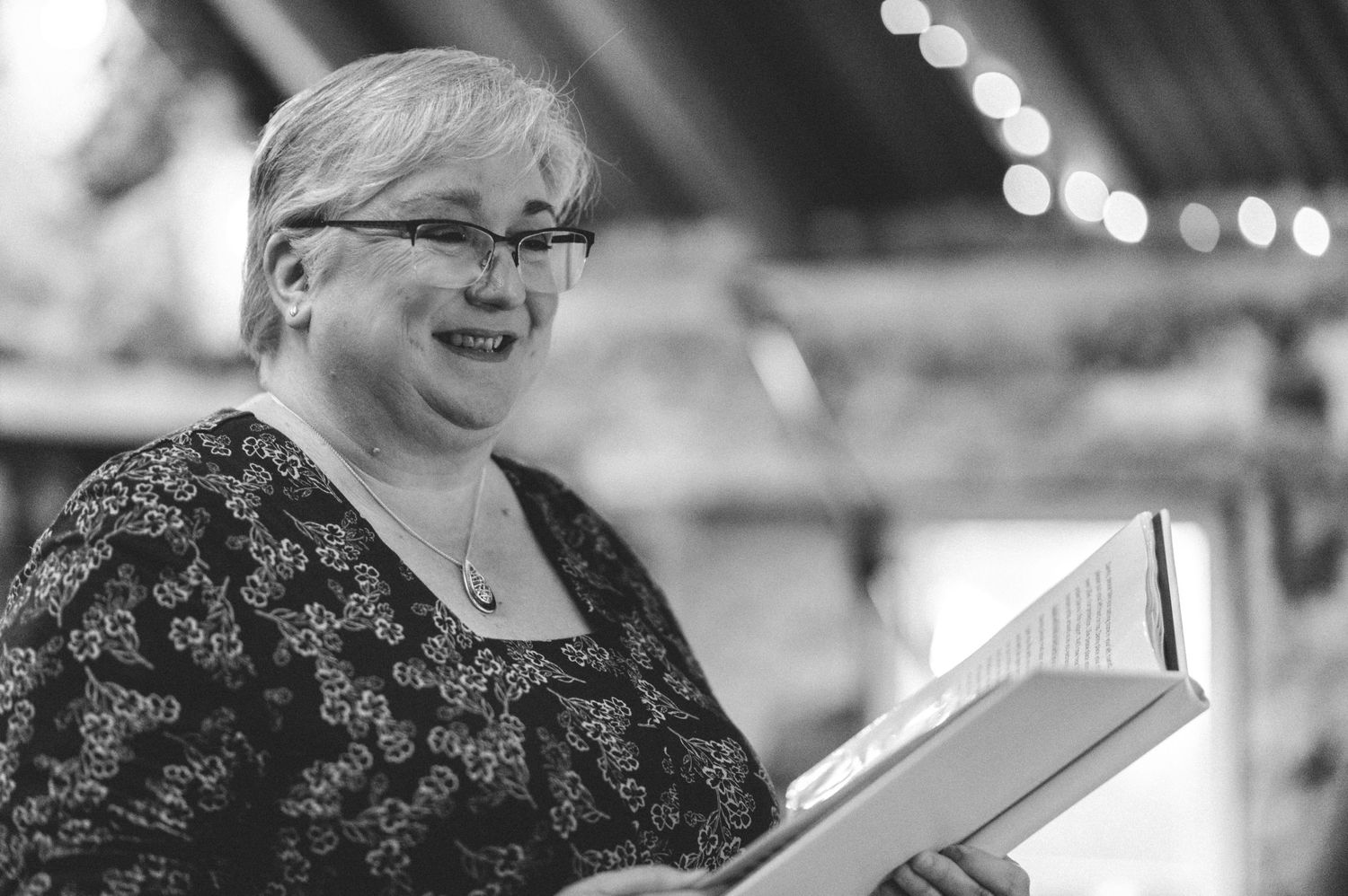 Black and white portrait of person holding open book while wearing patterned top.