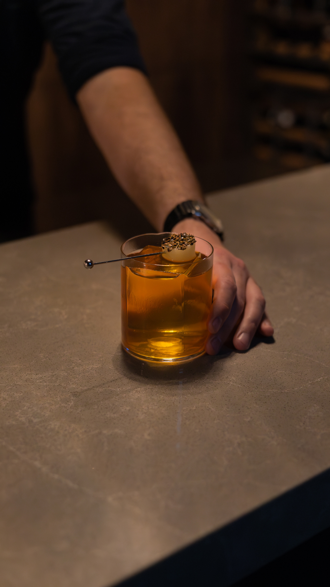 Amber-colored cocktail garnished with caviar served on a stone surface.