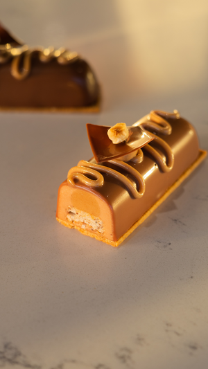 Close-up of a luxurious caramel-glazed chocolate bar with decorative toppings on a marble surface.