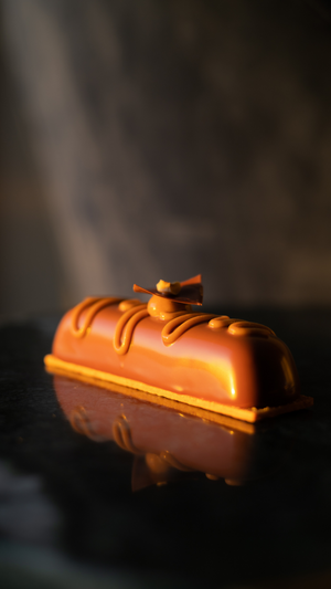 Elegant chocolate bar with caramel glaze and decorative drizzle on a reflective black surface in moody lighting.