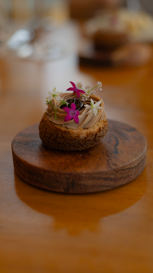 An elegant choux pastry decorated with pink flowers and cream on a wooden serving board.