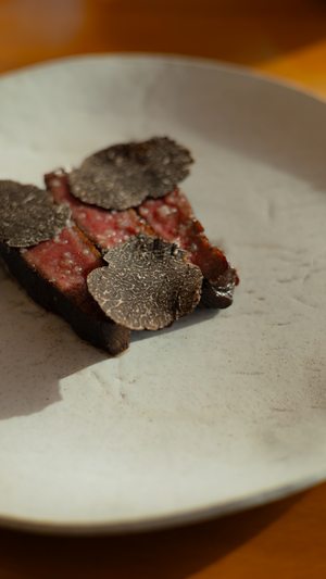 Sliced meat garnished with fresh black truffle shavings on a white ceramic plate.
