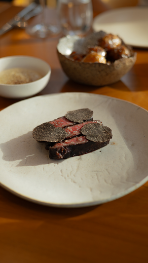 A plated dish featuring sliced meat topped with shaved black truffles on a white plate.
