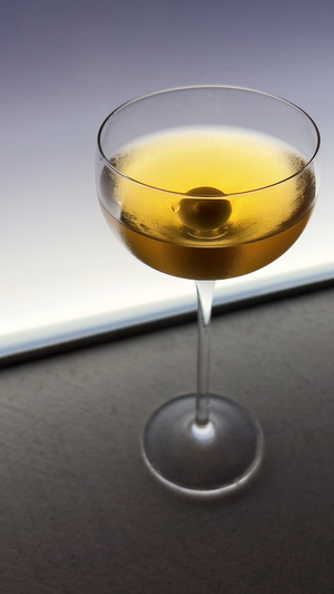 An elegant coupe glass filled with amber-colored cocktail and spherical garnish.