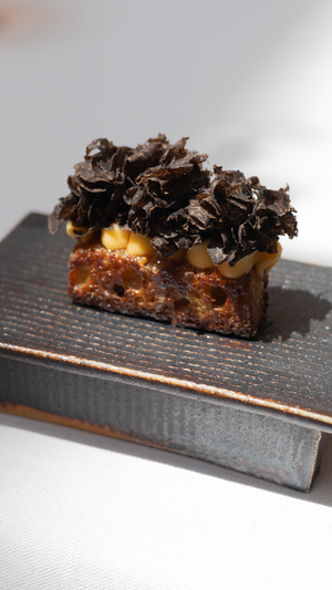 A decadent chocolate dessert with shaved dark chocolate topping on a textured black serving board.