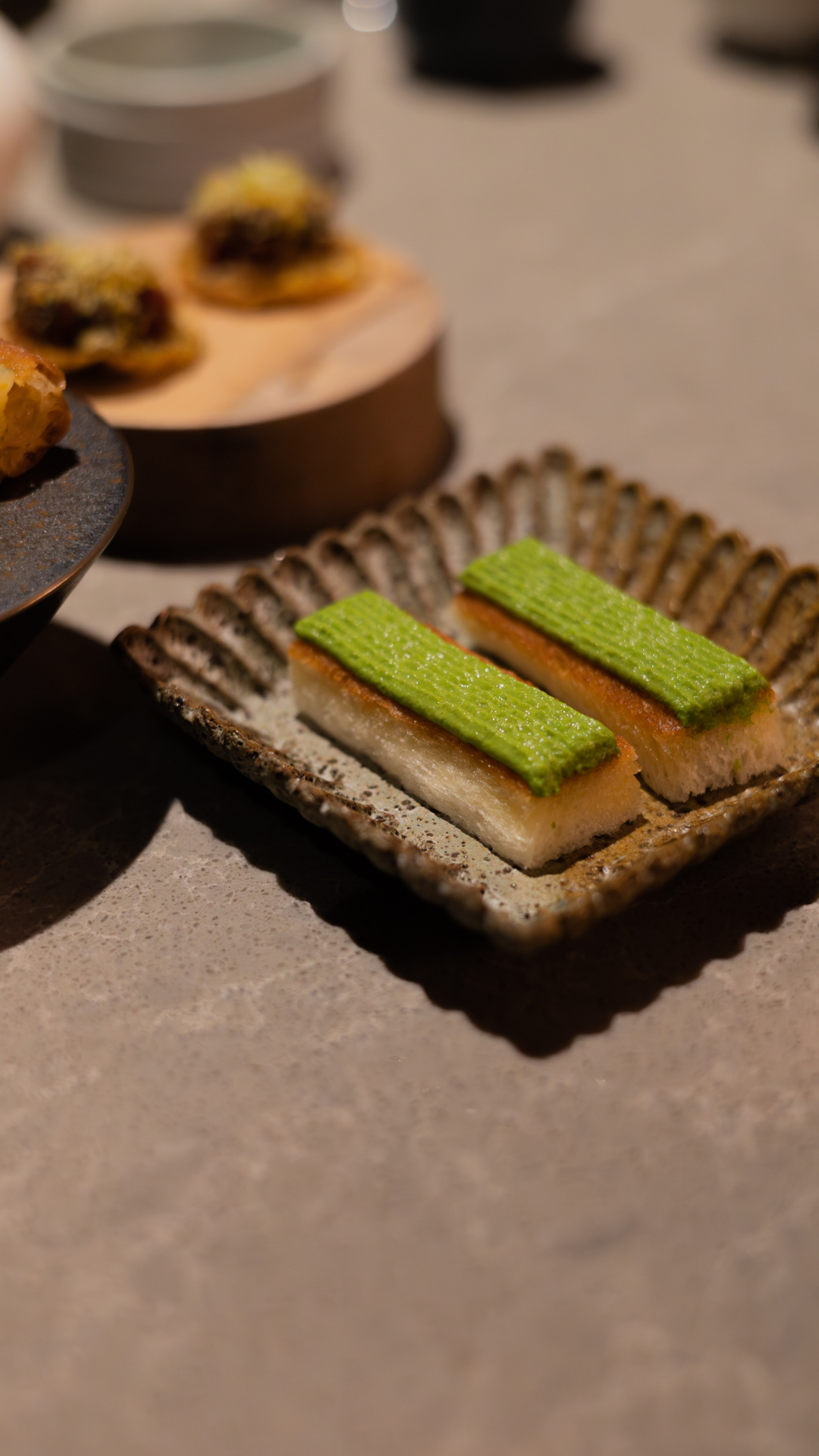Vibrant green tea bars served on a textured ceramic plate alongside other desserts.