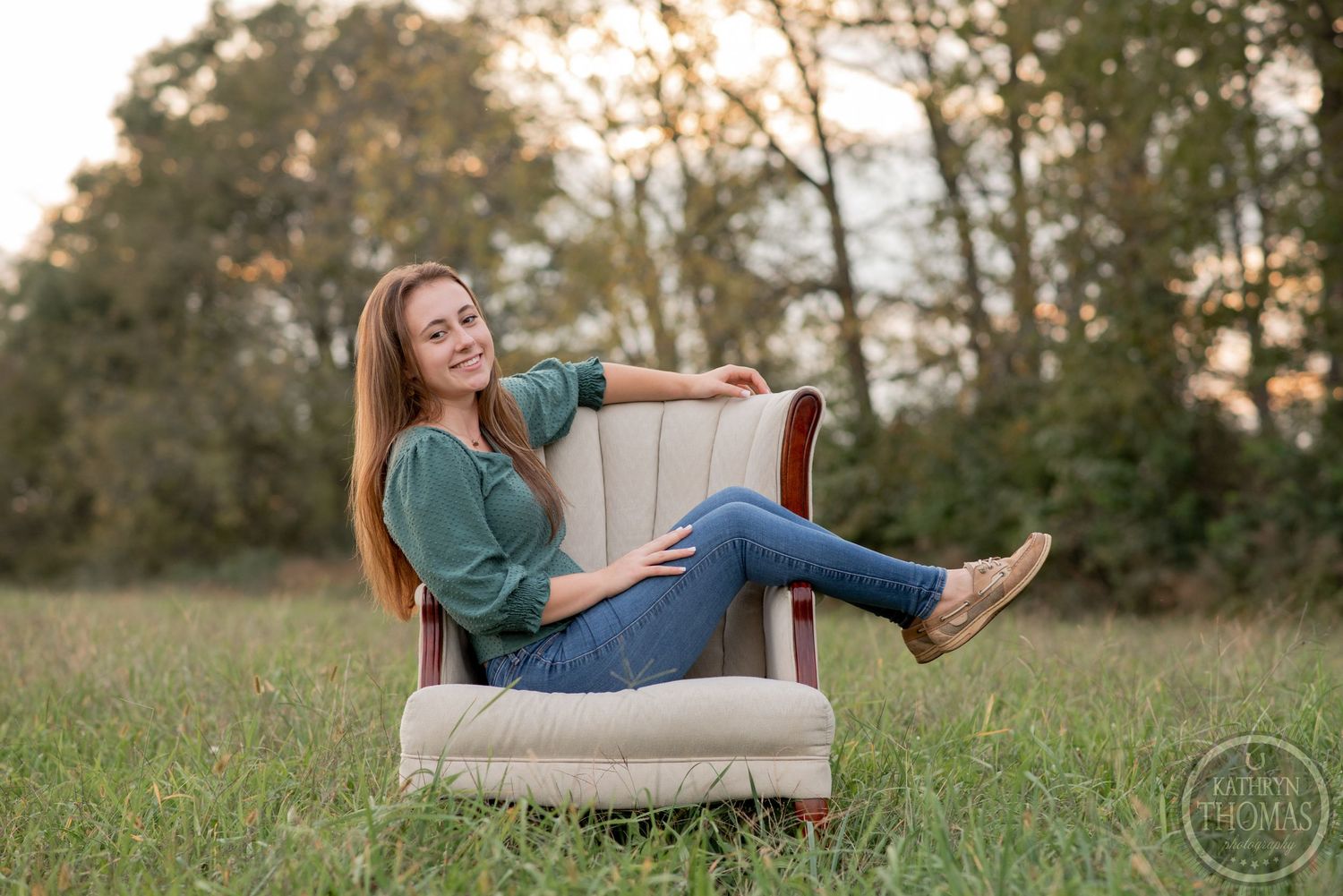A casual outdoor portrait session featuring a comfy beige armchair in a grassy field at sunset.