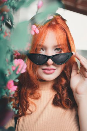 Artistic fashion photo with black cat-eye sunglasses framed by pink blossoms.
