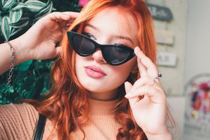 Close-up fashion portrait with black sunglasses and green botanical elements.