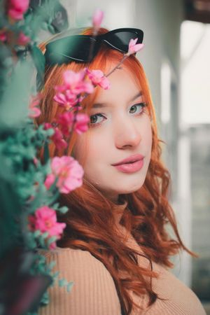 Dreamy portrait with pink flowers and sunglasses perched on vibrant red hair.