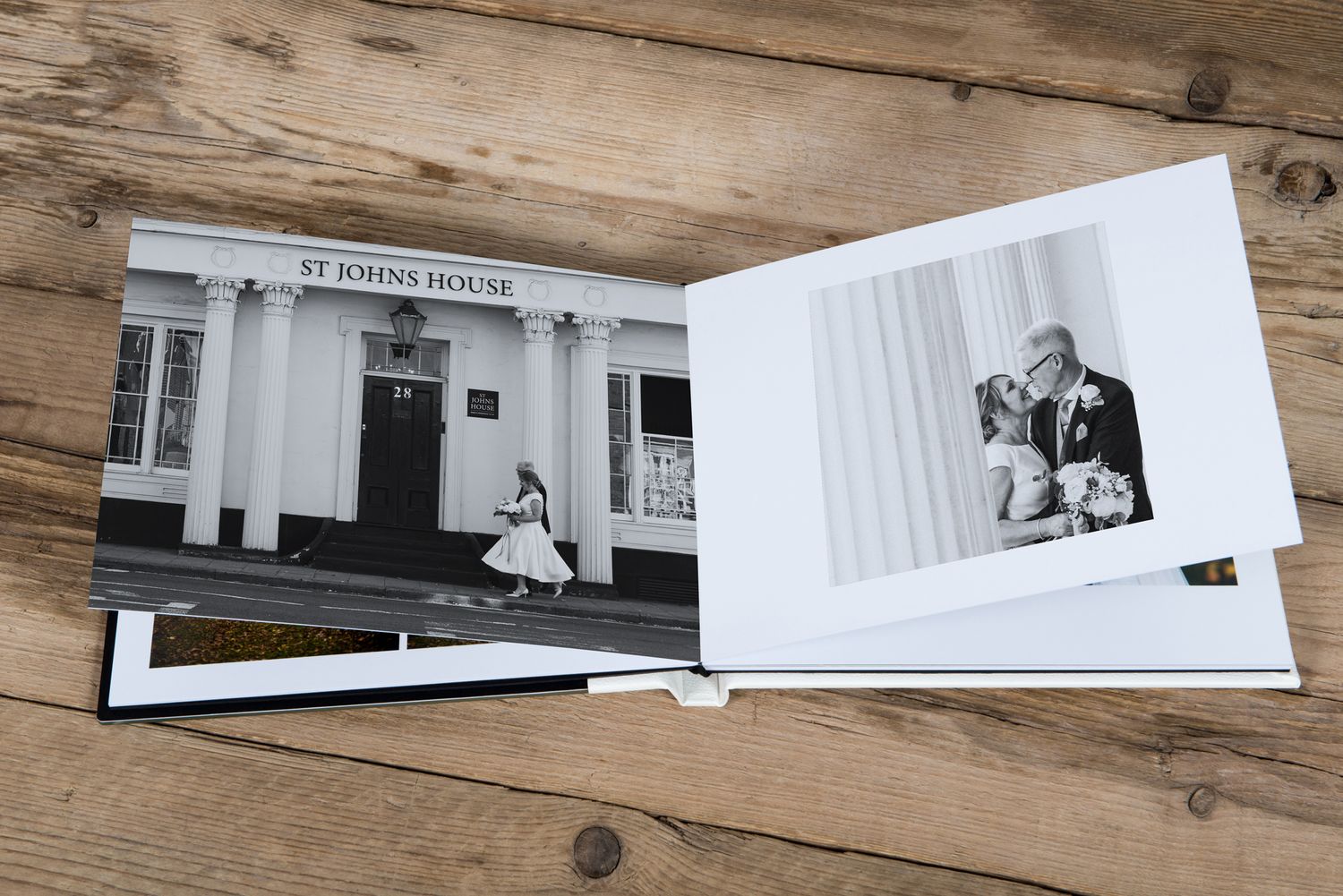 Black and white wedding photos displayed in an elegant photo album on wooden surface.