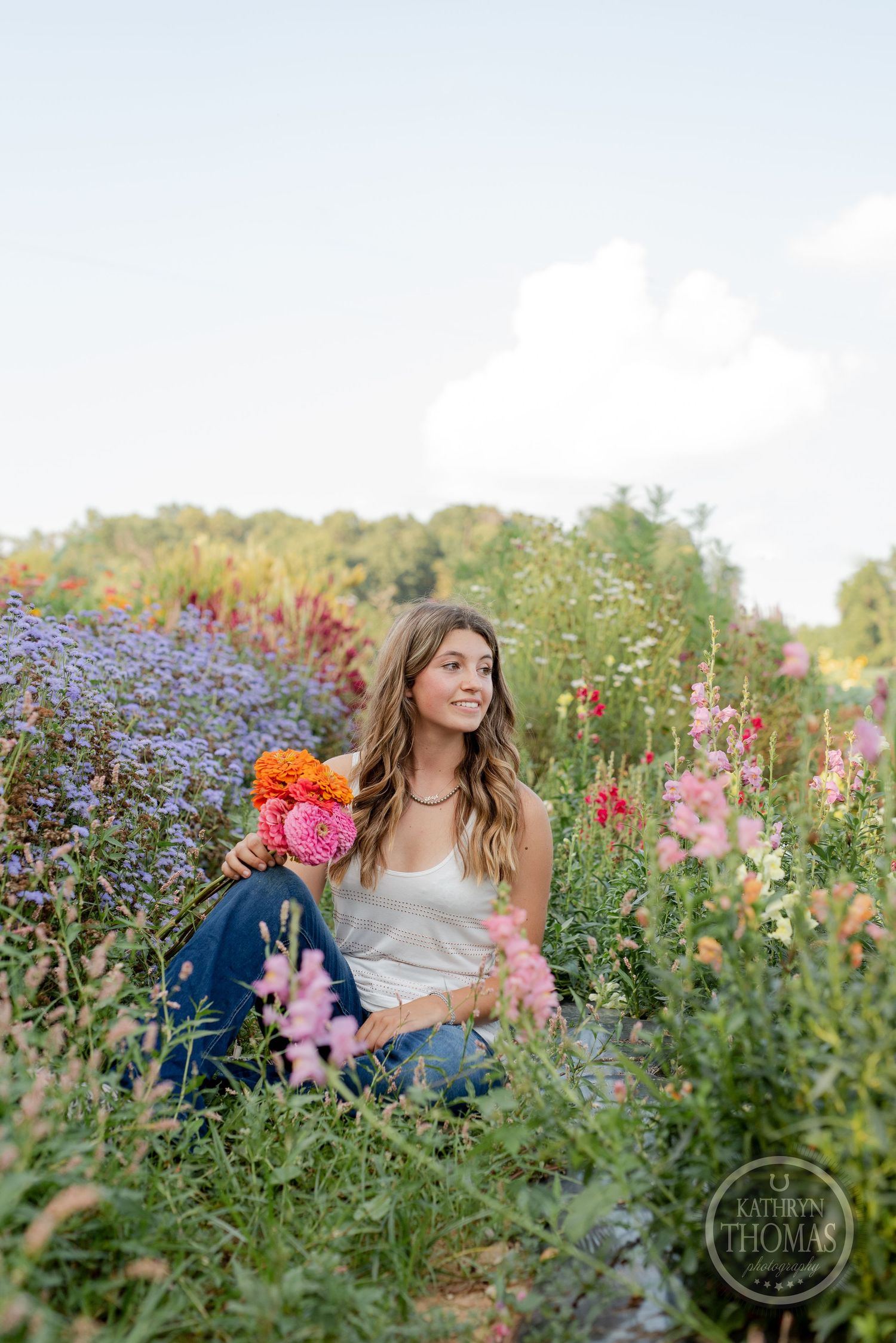 Person holding orange flowers while sitting among purple asters in summer garden.