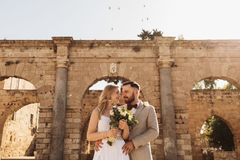 Bride and groom sharing a romantic moment beneath ancient stone arches at wedding.